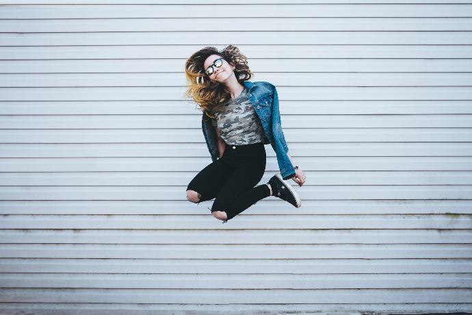 woman jumping in front of white concrete establishment